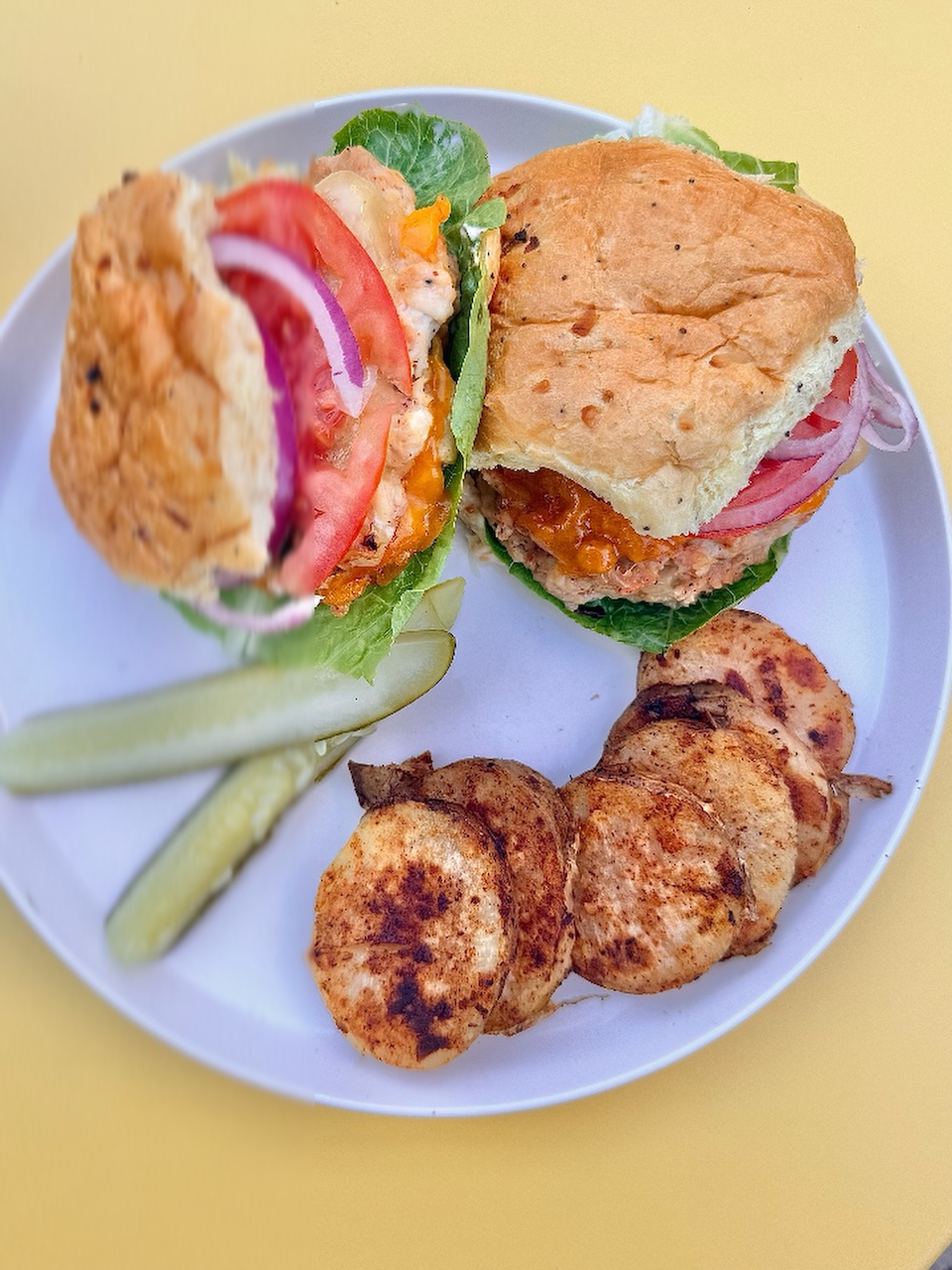 Ground chicken burger plated with grilled potato rounds and a pickle spear